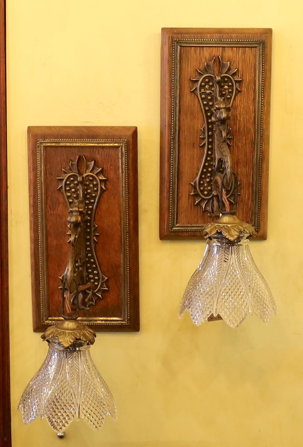 A pair of early 20th century English bronze metal dragon pendant wall lights, with moulded glass shades and mahogany back plates, height overall 35cm